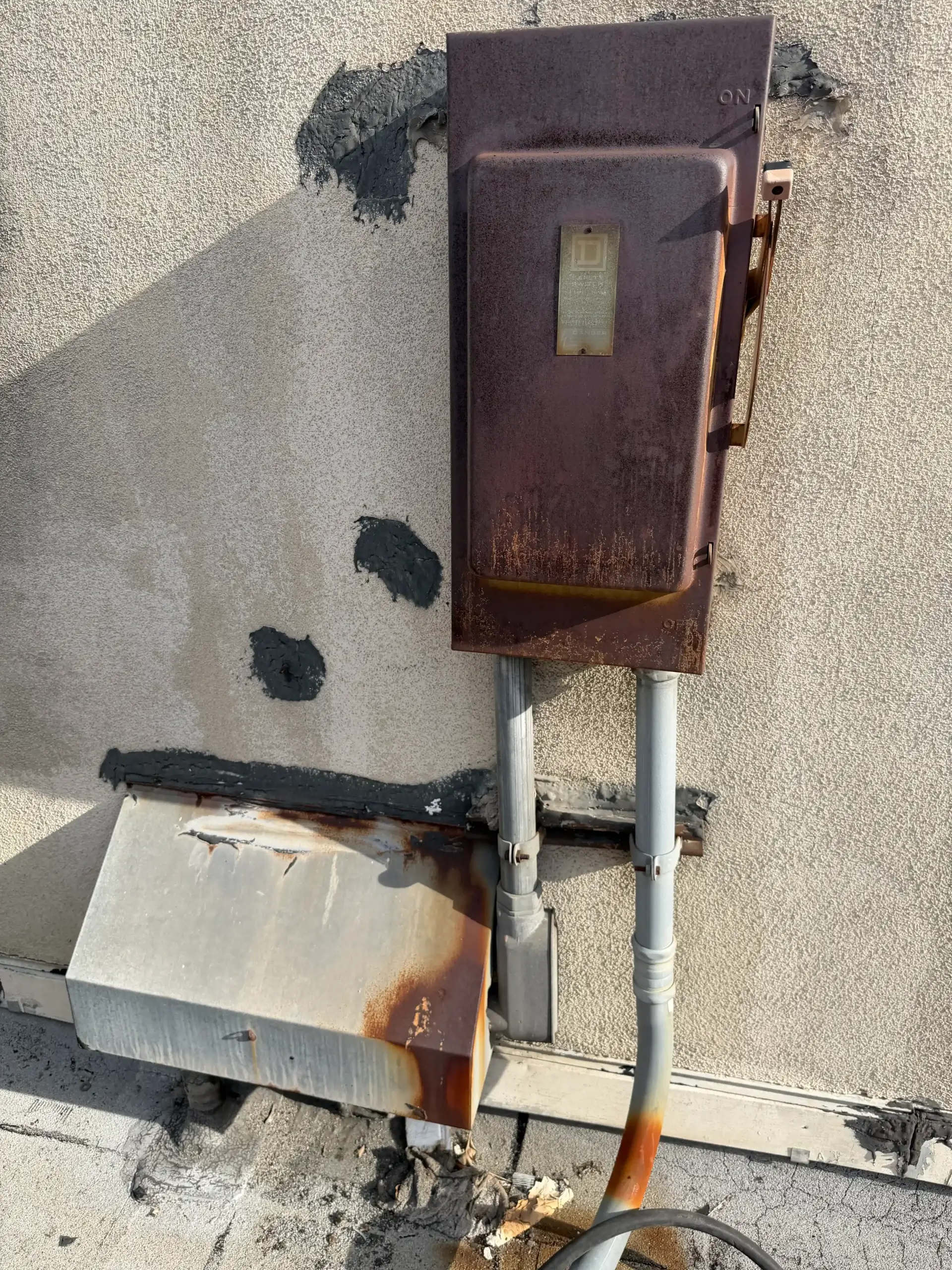 Rusty outdoor electrical disconnect box with conduit and corrosion stains on wall
