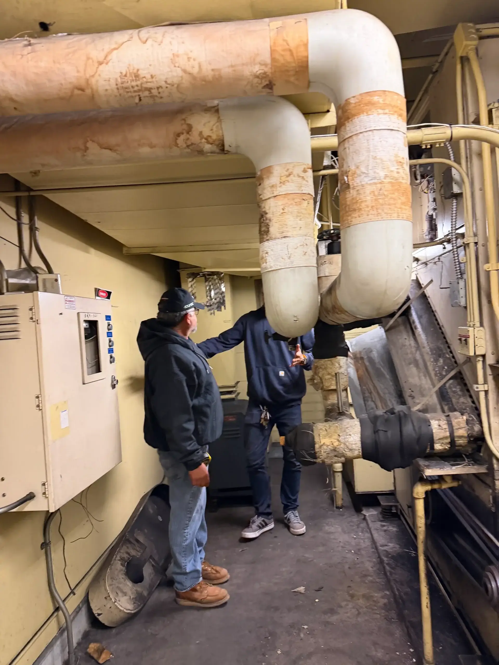 Technicians inspecting HVAC piping in mechanical room